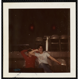 A girl and a boy posing with their arms behind their heads while sitting in front of a stage at the South Boston Boys' Club