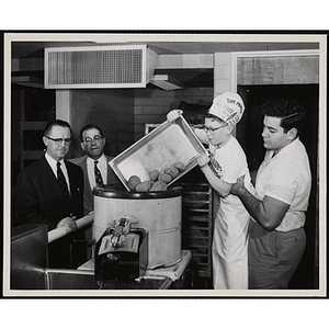 Hoisted by a Brandeis University kitchen staff member, a member of the Tom Pappas Chefs' Club dumps potatoes into a hopper as Chairman of Chefs Club Committee Alexander Armour (far left) and Chefs Club Committee member and Director of Brandeis University Dining Halls Norman R. Grimm (second from left) look on