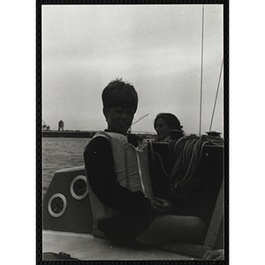 A boy sits on the deck of a sailboat in Boston Harbor