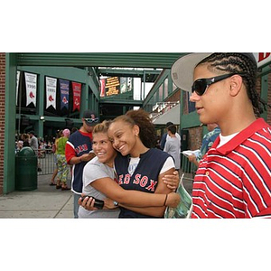 Two Torch Scholars pose together as a third stands nearby outside Fenway Park