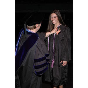 School of Nursing faculty member pins a ribbon to a student's graduation robe at pinning ceremony during convocation