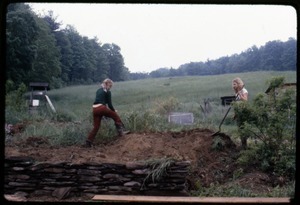 Janice Frey (right) and Sue Kramer, digging in a flower bed by a stone wall, Montague Farm Commune
