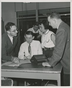 Unidentified man demonstrating his profession for three onlookers