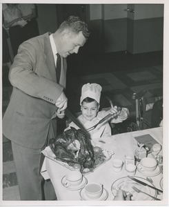 Willis C. Gorthy carving turkey with young client at Thanksgiving party