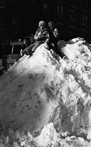 Unidentified children sitting on large snow pile