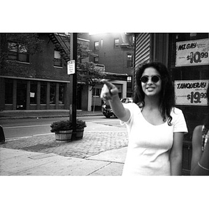 A young woman in sunglasses standing in front of a liquor store points to something down the street.