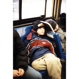 Little boy slumped in a city bus seat all bundled up for winter weather.