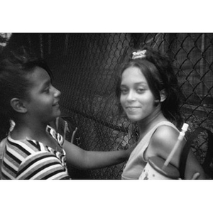 Two teenage girls by a chain link fence.