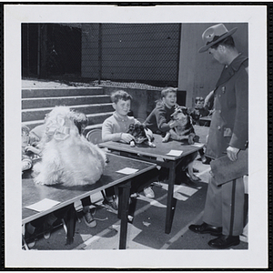 Two boys holding their dogs on the table as one of the judges stands in front of them during a Boys' Club Pet Show