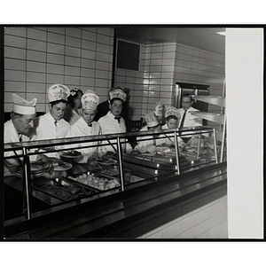 Members of the Tom Pappas Chefs' Club work the cafteria line in a Howard Johnson's as Chefs' Club Committee member Mary A. Sciacca (back row, left) and Brandeis University Director of Dining Halls and Chef's Club Committee member Norman R. Grimm (far right) look on