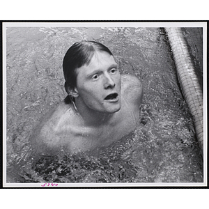 A teenage boy emerges from the water of a natatorium pool