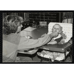 An Unidentified woman feeding a baby, who is stting in a high chair