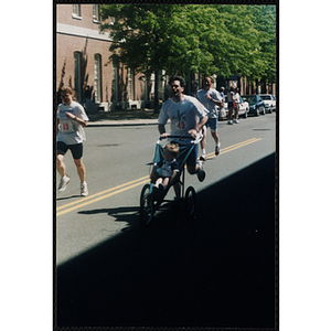 A man pushes a child in a stroller as he runs the Battle of Bunker Hill Road Race