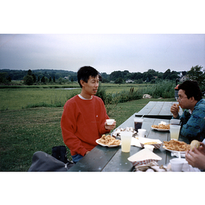 Young man sits at a picnic table and converses with others while eating