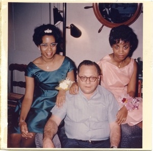 Bernie Moss seated on a sofa between two women