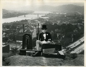 Clif Garboden: portrait on a hillside overlooking Pittsburgh, wearing top hat and sunglasses while holding soprano sax, and sign reading 'Soul brother'