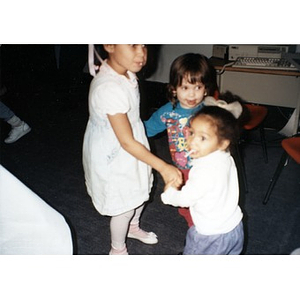 Three young children dancing together in a circle.