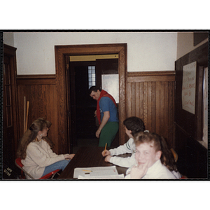 A young man enters a room in the Charlestown Boys and Girls Club while several other men and women sit around a table