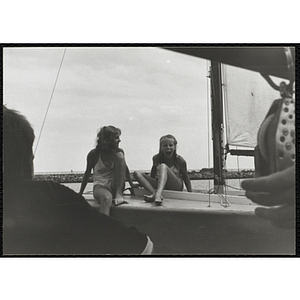Two teenage girls sit on the deck of a sailboat in Boston Harbor