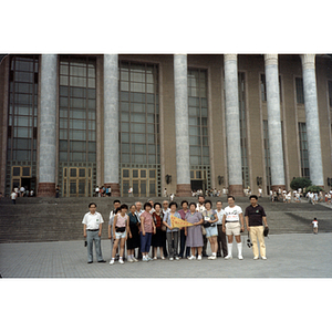 Men and women stand in a group in front of a large building with marble pillars