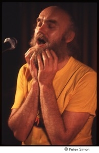 Ram Dass with his hands on his beard, on stage with Amazing Grace