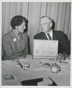 Bruce Barton and woman hold a certificate at the Institute for the Crippled and Disabled's 35th anniversary Red Cross luncheon