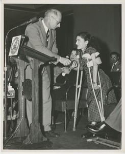 Unidentified staff member handing prize to client on crutches at Institute Day