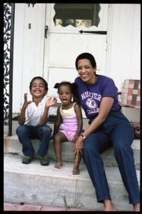 Johnnetta Cole seated on the front steps of a house, with Zena and Antonio Allen
