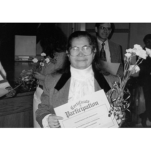 Woman holds a bouquet of carnations and a certificate of participation.