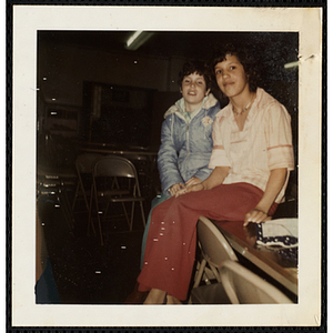 A girl and a boy sitting on a table and looking at the camera at the South Boston Boys' Club