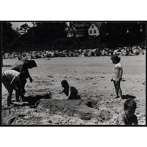 A man and three girls work on a sand sculpture on a beach