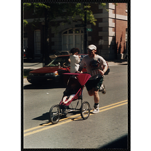 A man pushes a child in a stroller as he runs the Battle of Bunker Hill Road Race