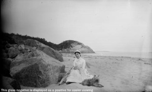 Mrs. Jim Scott and dog seated by rock at east end of Singing Beach, Manchester