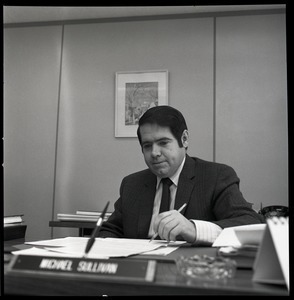 Michael Sullivan seated at his desk, pen in hand: Treasurer's Office, University of Massachusetts