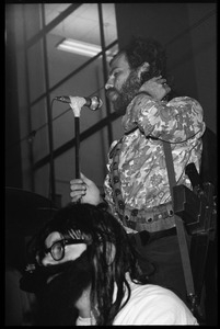 Jerry Rubin, with bandolier and toy assault rifle slung over his shoulder, addressing the audience at the microphone