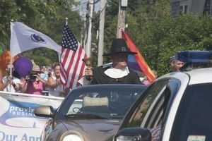 Police escort leading the approaching parade, with man dressed in Puritan costume ringing a bell : Provincetown Carnival parade