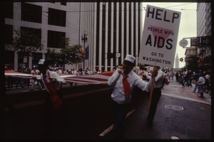Veteran carrying an American flag and sign reading 'Help people with AIDS go to Washington' in the San Francisco Pride Parade