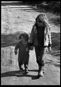 Child leading a toddler by hand along a dirt road, Earth People's Park