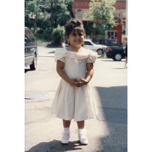 A little girl in a dress stands in the street