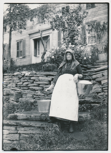 Wife of Curtis Burroughs stands with two pails at the homestead