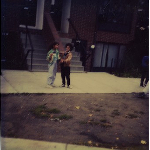 Two girls standing on the sidewalk in front of Villa Victoria row houses.