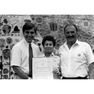 Michael Dukakis posing with a man and woman in front of the ceramic tile mural in the Plaza Betances.