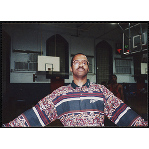 A staff member spreading his arms out while looking at the camera on a basketball court