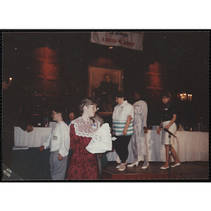 Julie Treanor holds a Boys and Girls Club t-shirt and looks to her left while several people stand in line in front of the head table at the "Recognition Dinner at Harvard Club"