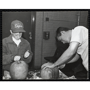 A man and a boy carve pumpkins at a Halloween event