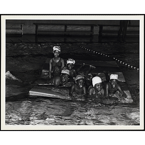 A group of girls pose for a shot on a flotation device in a natatorium pool