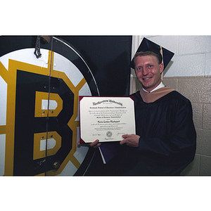 Standing by a Boston Bruins banner in his academic robes, Nevin Markwart of the Bruins poses with his diploma