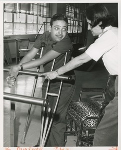 Luis Damilano using parallel bars with assistance from a physical therapist