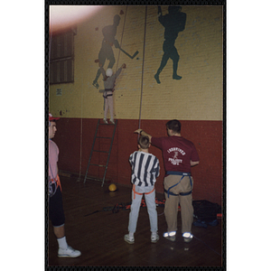 An indoor climbing supervisor holds a safety rope for a girl climbing up a wall