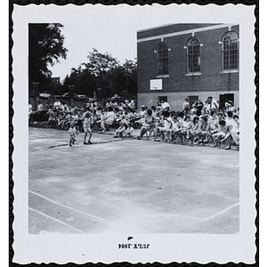 Participants and their families sit and stand in a playground during a Boys' Club Little Sister Contest